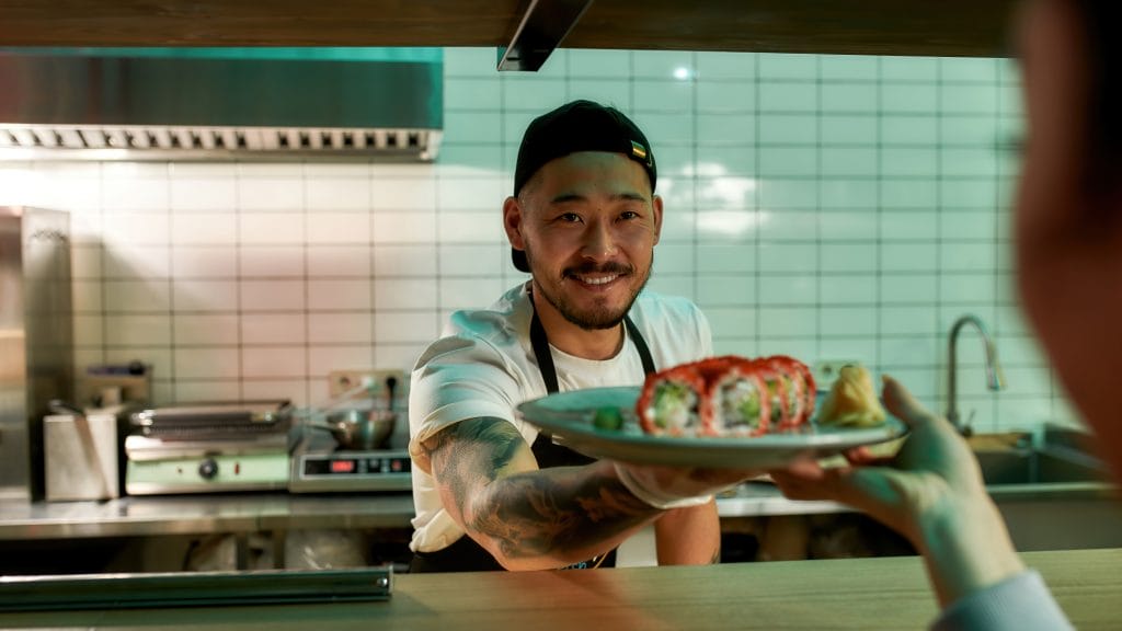 A male Asian Sushi Chef handing over a plate of maki rolls