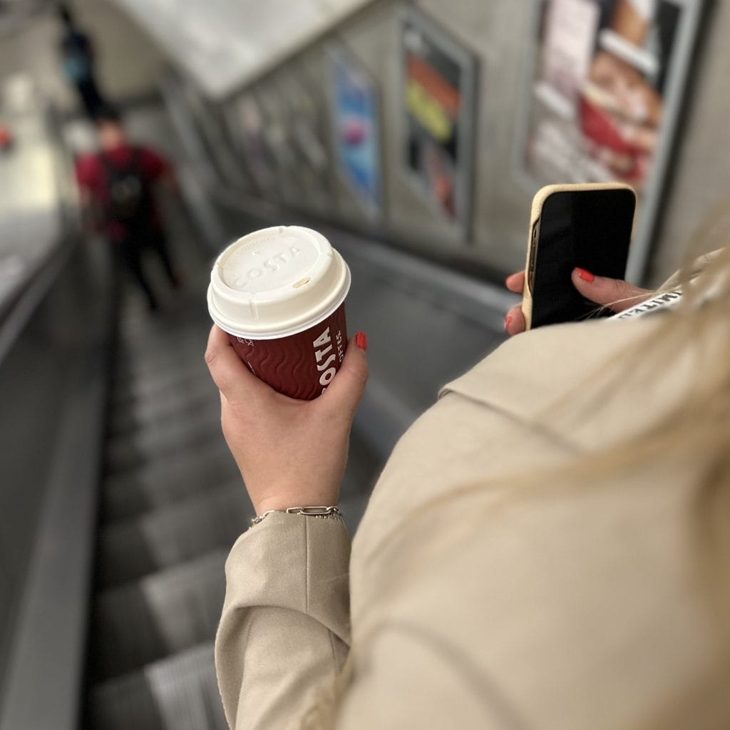 a women on an escalator holding a Costa Coffee paper cup