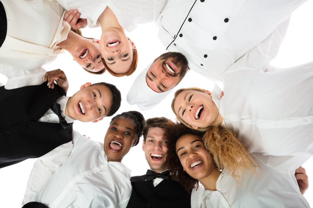 restaurant staff standing in a circle, hugging and smiling to the camera;  how to motivate restaurant employees