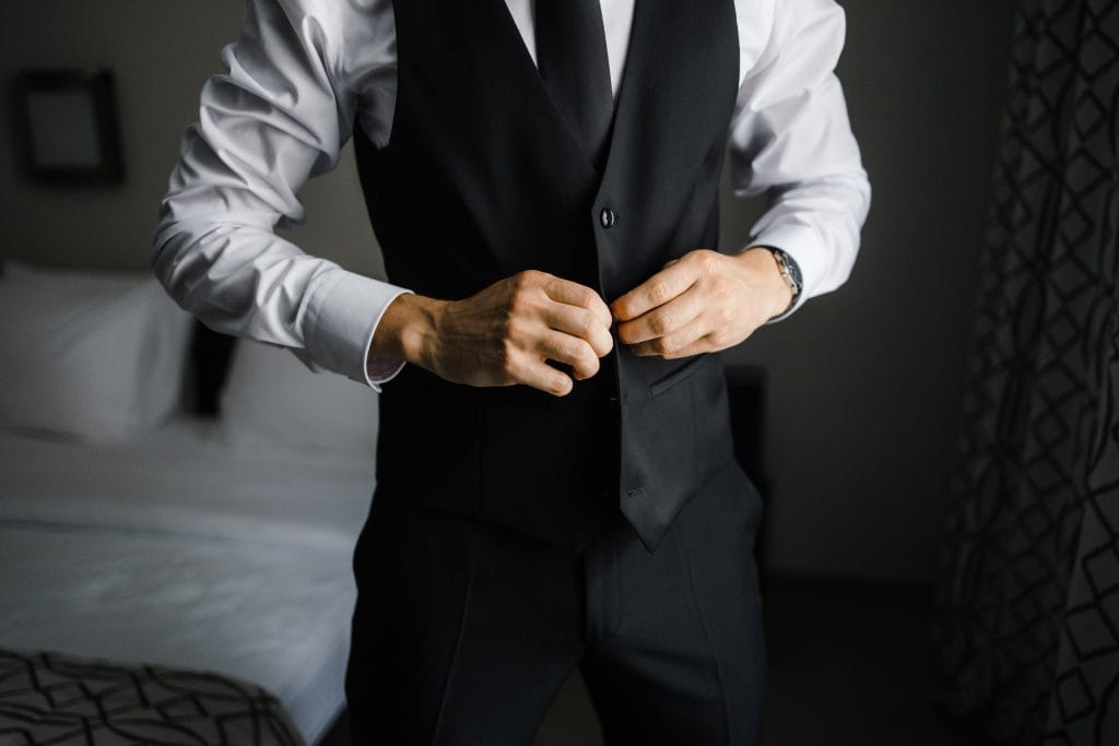 man putting on a black formal vest; fine dining server dress code