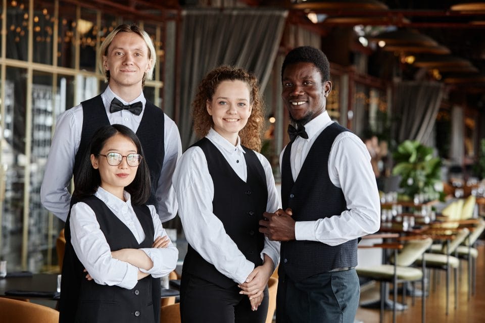 four fine dining servers wearing white shirts and black vests