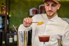 bartender garnishing a cocktail with a dehydrated orange slice