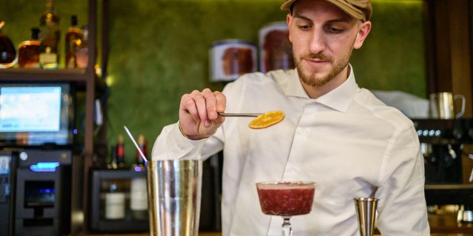 bartender garnishing a cocktail with a dehydrated orange slice