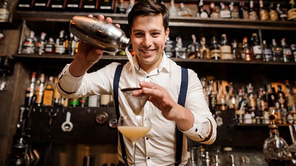 An image of a smiling bartender preparing a cocktail; best paying restaurant jobs