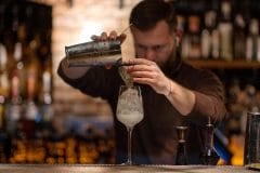 bartender pouring a cocktail into a glass