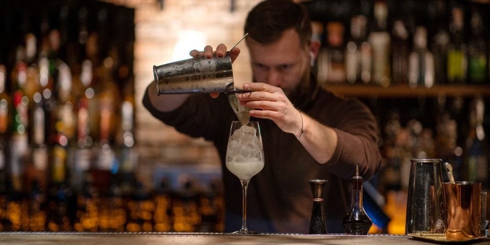 bartender pouring a cocktail into a glass