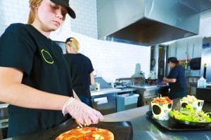 young cook prepping pizza in a restaurant kitchen