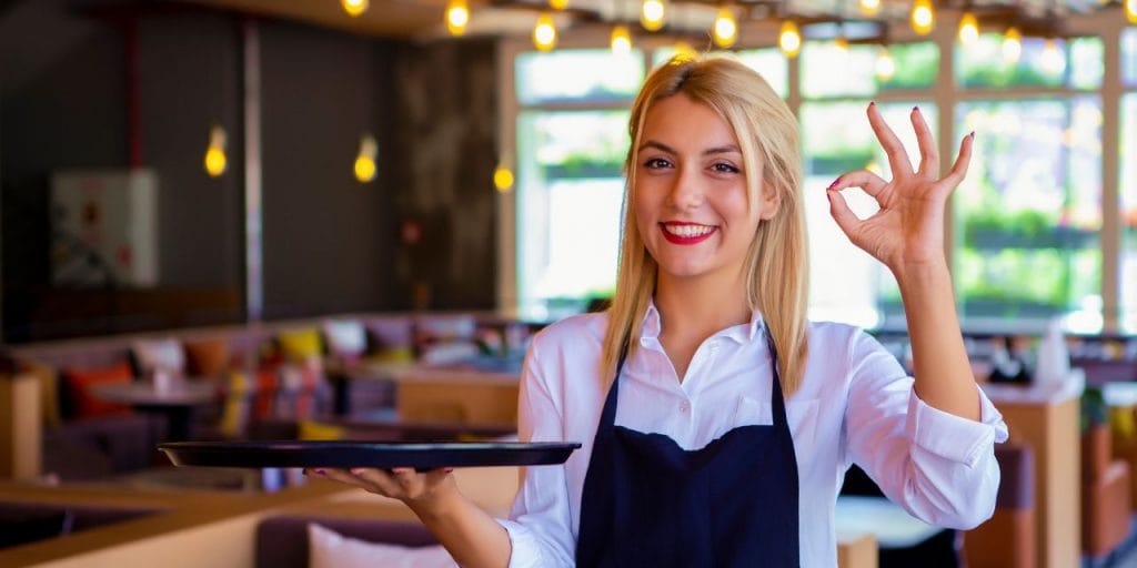 a smiling waitress showing the A-OK sign while holding a tray